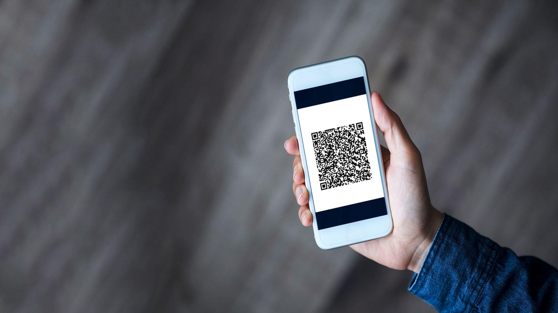 Handy in der Hand eines Mannes, Screen zeigt QR-Code