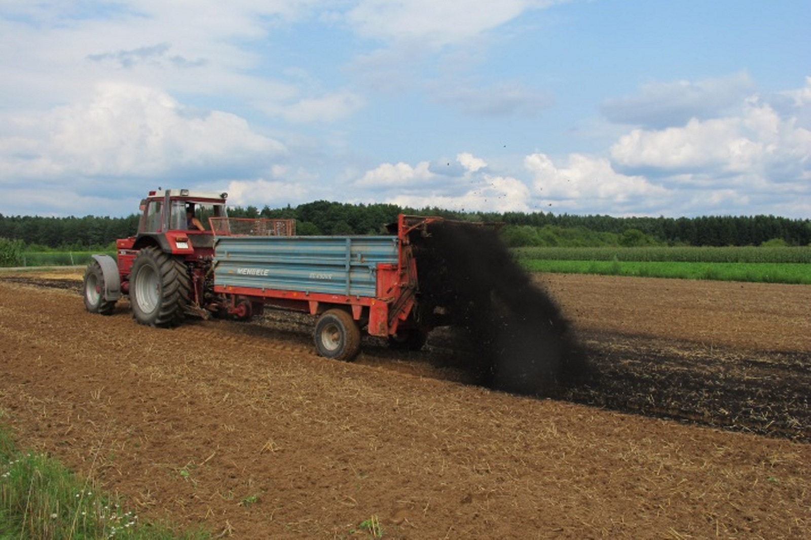 Traktor mit Anhänger schüttet Biokohle auf Acker